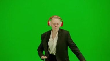 İş kadını kulaklıkla müzik dinliyor ve neşeyle dans ediyor. İş elbiseli kadın yeşil ekranda kromakey ile. Modern iş kadını yaratıcı reklam konsepti.