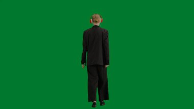 Modern iş kadını yaratıcı reklam konsepti. Krom anahtar yeşil ekranda takım elbiseli kadın portresi. Resmi kıyafetli sarışın iş kadını kulaklıkla yürüyor akıllı telefondan müzik dinliyor.