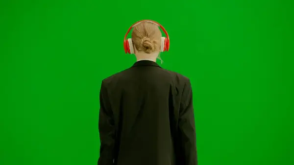 Modern businesswoman creative advertisement concept. Portrait of female in suit on chroma key green screen. Blonde business woman in formal outfit walking in headphones listening music on smartphone