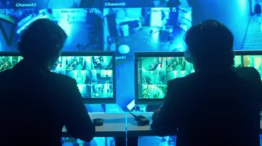 Gözetleme ve güvenlik konsepti. İzleme merkezinde çalışan erkek güvenlik görevlileri telsizle konuşuyor ve tartışıyorlar. Bilgisayarlar ve büyük dijital ekran kamera görüntüleri.