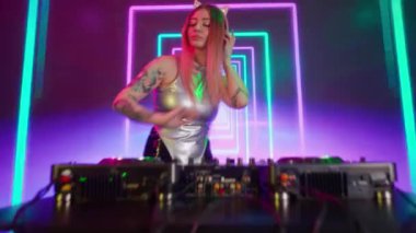 Gelecekçi siber punk teknolojisi konsepti. Dijital duvar renkli görsel arka planda çekici bir kadın. Genç kadın DJ dans ediyor, pikaplarda müzik çalıyor gece kulübünde mikser yapıyor, kameraya bakıyor..