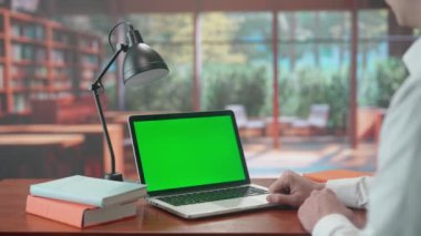 Adamın biri laptoptan yeşil ekranlı bir video üzerinden iletişim kuruyor. Pencereli sıcak kütüphane arkaplanı. Metin veya resim için şablon yeri, promosyon içeriği. Reklam alanı çalışma alanı modeli
