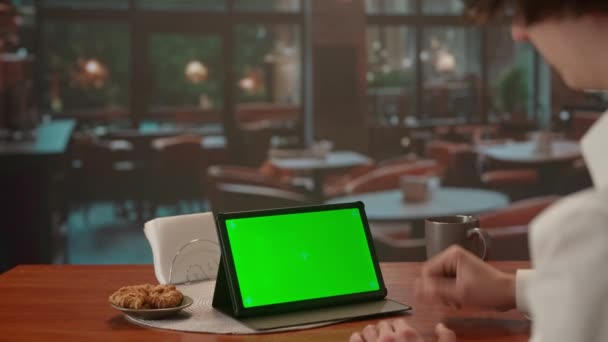 男人在视频通话中使用绿色屏幕平板电脑 晚上在有大窗户的咖啡店里 模板的位置为您的文字或形象 促销内容 广告区 模拟工作区 — 图库视频影像