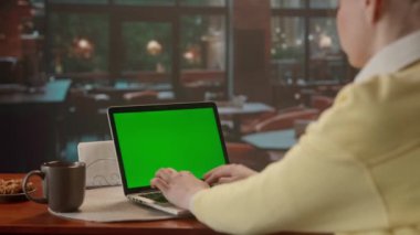 Laptop klavyesinde yeşil ekranlı bir kadın. Büyük pencereli kafede akşam yemeği. Metin veya resim için şablon yeri, promosyon içeriği. Reklam alanı, çalışma alanı maketi