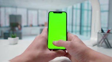 Mans elleri akıllı telefon yeşil ekran kroma anahtarıyla etkileşimde. Pencereleri olan parlak bir ofis. Metin veya resim için şablon yeri, promosyon içeriği. Reklam alanı, çalışma alanı maketi.