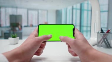 Akıllı telefon yeşil ekran krom anahtarıyla mesaj atan bir adamın elleri. Pencereleri olan parlak bir ofis. Metin veya resim için şablon yeri, promosyon içeriği. Reklam alanı, çalışma alanı maketi.