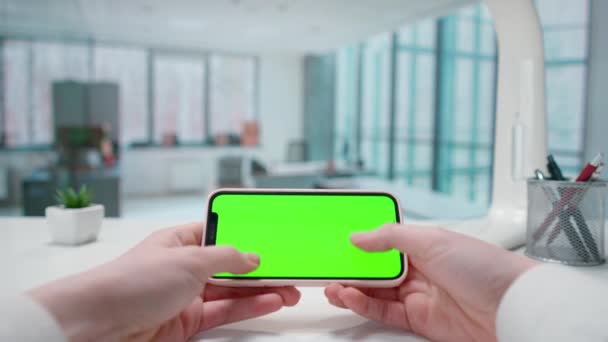 スマートフォンの緑色のクロマキーにテキストを送信する女性の手 窓のある明るいオフィス テキストや画像 プロモーションコンテンツのテンプレート 広告エリア ワークスペースモックアップ — ストック動画
