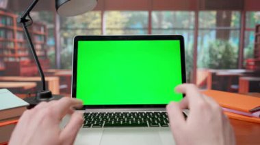 Adamın biri laptoptan yeşil ekranlı bir video üzerinden iletişim kuruyor. Pencereli sıcak kütüphane arkaplanı. Metin veya resim için şablon yeri, promosyon içeriği. Reklam alanı çalışma alanı modeli
