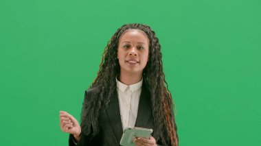 Televizyon haberleri ve canlı yayın konsepti. Genç bayan muhabir krom anahtar yeşil ekran arka planında izole edildi. Afrika kökenli Amerikalı kadın televizyon sunucusu elinde tabletle yürüyor ve konuşuyor..