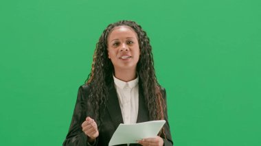 Televizyon haberleri ve canlı yayın konsepti. Genç bayan muhabir krom anahtar yeşil ekran arka planında izole edildi. Afrikalı Amerikalı kadın televizyon sunucusu konuşuyor ve gazete okuyor..