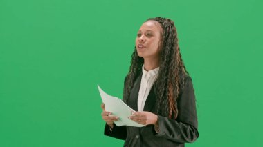 Televizyon haberleri ve canlı yayın konsepti. Genç bayan muhabir krom anahtar yeşil ekran arka planında izole edildi. Afrikalı Amerikalı kadın TV sunucusu konuşuyor ve gazete okuyor. Yarım dönüş..