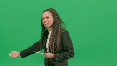 Televizyon haberleri ve canlı yayın konsepti. Genç bayan muhabir krom anahtar yeşil ekran arka planında izole edildi. Afro-Amerikan TV haber sunucusu elinde tablet, boş bir alan gösteriyor..