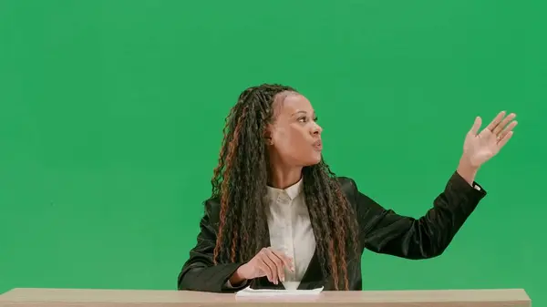 テレビニュースとライブ放送コンセプト クロマキーの緑色の背景に隔離された机の女性の記者 アフリカ系アメリカ人女性テレビのニュースホストがカメラで話している — ストック写真