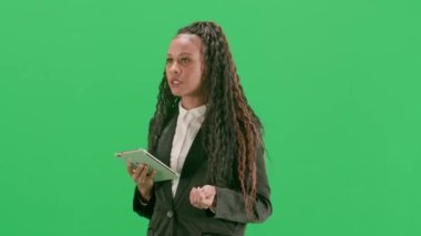 Televizyon haberleri ve canlı yayın konsepti. Genç bayan muhabir krom anahtar yeşil ekran arka planında izole edildi. Afro-Amerikalı kadın televizyon sunucusu elinde tabletle yürüyor ve konuşuyor. Yarım dönüş..