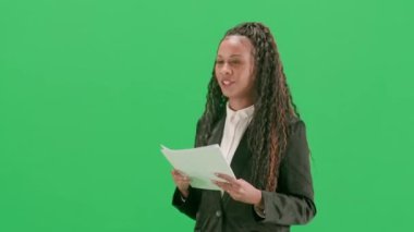Televizyon haberleri ve canlı yayın konsepti. Genç bayan muhabir krom anahtar yeşil ekran arka planında izole edildi. Afrikalı Amerikalı kadın TV sunucusu konuşuyor ve gazete okuyor. Yarım dönüş..