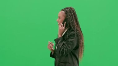 Televizyon haberleri ve canlı yayın konsepti. Genç bayan muhabir krom anahtar yeşil ekran arka planında izole edildi. Afrika kökenli Amerikalı kadın televizyon sunucusu akıllı telefondan konuşuyor. Yan görünüm.
