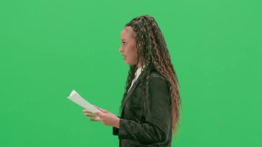 Televizyon haberleri ve canlı yayın konsepti. Genç bayan muhabir krom anahtar yeşil ekran arka planında izole edildi. Afrikalı Amerikalı kadın TV sunucusu konuşuyor ve gazete okuyor. Yan görünüm.
