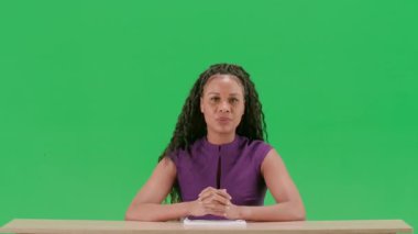 Televizyon haberleri ve canlı yayın konsepti. Elbiseli bir kadın, krom anahtar yeşil ekran arka planında izole bir şekilde masada oturuyor. Afrika kökenli Amerikalı kadın TV sunucusu oturmuş kameraya bakıyor..