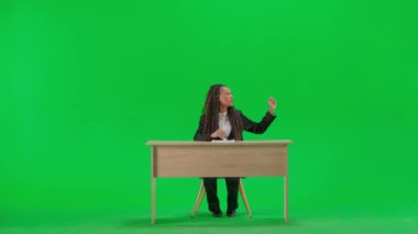 Televizyon haberleri ve canlı yayın konsepti. Masadaki kadın muhabir krom anahtar yeşil ekran arka planında izole edilmiş. Tam teşekküllü Afro-Amerikan kadın TV sunucusu oturmuş kameraya bakıyor..