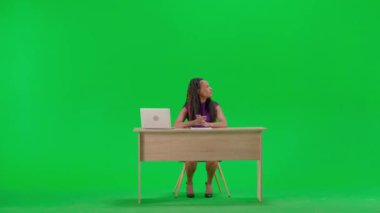 Televizyon haberleri ve canlı yayın konsepti. Elbiseli bir kadın, krom anahtar yeşil ekran arka planında izole bir şekilde masada oturuyor. Tam teşekküllü Afro-Amerikan kadın TV sunucusu, online muhabirle konuşuyor..