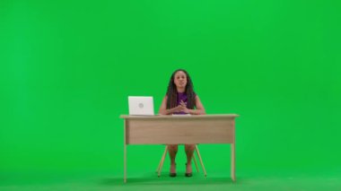 Televizyon haberleri ve canlı yayın konsepti. Elbiseli bir kadın, krom anahtar yeşil ekran arka planında izole bir şekilde masada oturuyor. Tam teşekküllü Afro-Amerikan kadın TV sunucusu oturmuş kameraya bakıyor..