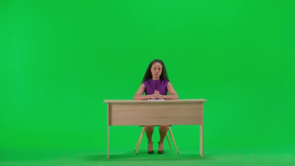 テレビニュースとライブ放送コンセプト ドレスの女性は クロマキーグリーンスクリーンの背景に隔離された机に座ります フルショットアフリカ系アメリカ人女性テレビニュースホスト座ってカメラを見ている — ストック動画
