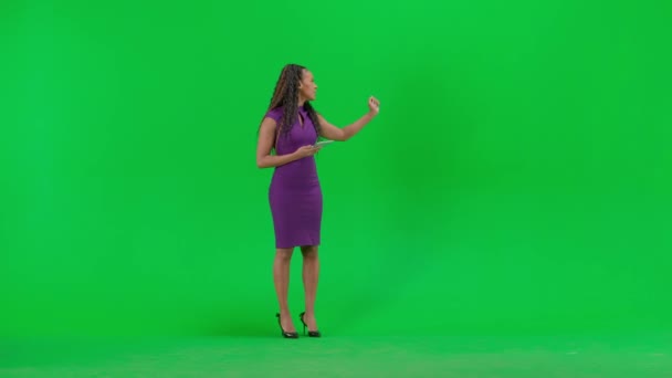 テレビニュースとライブ放送コンセプト クロマキーの緑色の背景に隔離されたドレスの女性 フルショット アフリカ系アメリカ人女性テレビニュースホストとタブレット立ってカメラを見ている — ストック動画