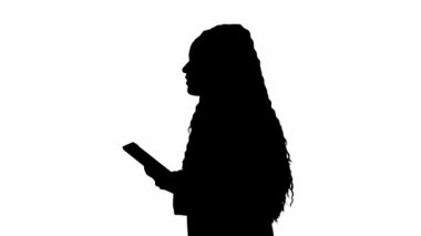 Televizyon haberleri ve canlı yayın konsepti. Genç bayan muhabir. Afro-Amerikalı kadın televizyon sunucusu elinde tabletle yürüyor ve konuşuyor. Beyaz arka planda siyah siluet. Yan görünüm.