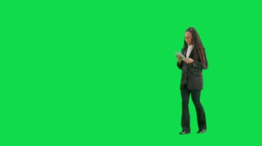 Televizyon haberleri ve canlı yayın konsepti. Genç bayan muhabir krom anahtar yeşil ekran arka planında izole edildi. Tam teşekküllü Afro-Amerikan kadın televizyon sunucusu elinde tabletle yürüyor ve konuşuyor. Yarım dönüş.