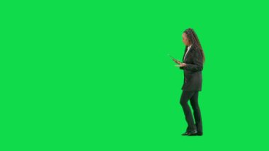 Televizyon haberleri ve canlı yayın konsepti. Genç bayan muhabir krom anahtar yeşil ekran arka planında izole edildi. Tam teşekküllü Afro-Amerikan kadın televizyon sunucusu elinde tabletle yürüyor ve konuşuyor. Yan görünüm