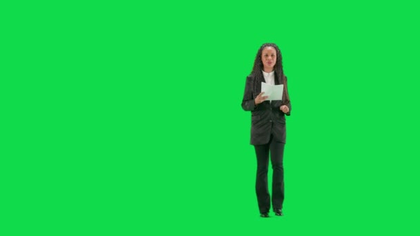 电视新闻和现场直播的概念 年轻的女记者在彩色键绿色屏幕背景上被隔离 全镜头非洲裔美国妇女电视新闻节目主持人走在谈话和阅读报纸 — 图库视频影像