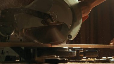 Marangozluk ve el işi reklam konsepti. Garajda çalışan erkek marangoz. Atölyede ahşap malzemelerle çalışan profesyonel marangoz uzmanı. Tahta kesmek için testere kullanıyor..