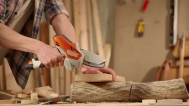 Marangozluk ve el işi reklam konsepti. Garajda çalışan erkek marangoz. Profesyonel marangoz, atölyede ahşap malzemelerle çalışıyor. Kablosuz testereyle odun kesiyor..