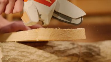 Marangozluk ve el işi reklam konsepti. Garajda çalışan erkek marangoz. Profesyonel marangoz atölyede malzemelerle çalışıyor. Kablosuz testereyle odun kesiyor. Kapatın..