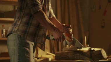 Marangozluk ve el işi reklam konsepti. Garajda çalışan erkek marangoz. Profesyonel marangoz, atölyede ahşap malzemelerle çalışıyor. Kablosuz testereyle odun kesiyor..