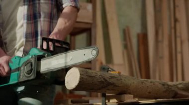 Marangozluk ve el işi reklam konsepti. Garajda çalışan erkek marangoz. Profesyonel marangoz, atölyede ahşap malzemelerle çalışıyor elektrikli testere kullanarak tahta kesiyor..