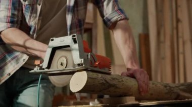 Marangozluk ve el işi reklam konsepti. Garajda çalışan erkek marangoz. Profesyonel marangoz, atölyede ahşap malzemelerle çalışıyor. Elektrikli testere kullanarak odun kesiyor..