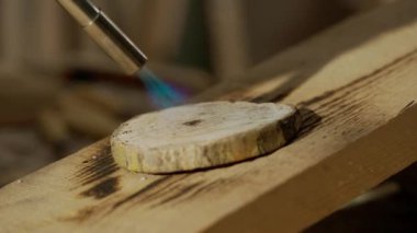 Marangozluk ve el işi reklam konsepti. Garajda çalışan erkek marangoz. Profesyonel marangoz, atölyede ahşap malzemelerle çalışıyor. Meşale ile odun yakıyor..