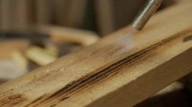 Marangozluk ve el işi reklam konsepti. Garajda çalışan erkek marangoz. Profesyonel marangoz, atölyede ahşap malzemelerle çalışıyor. Meşale ile odun yakıyor..