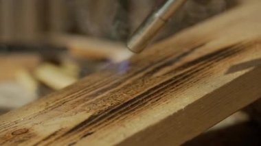 Marangozluk ve el işi reklam konsepti. Garajda çalışan erkek marangoz. Profesyonel marangoz, atölyede ahşap malzemelerle çalışıyor. Meşale ile odun yakıyor..