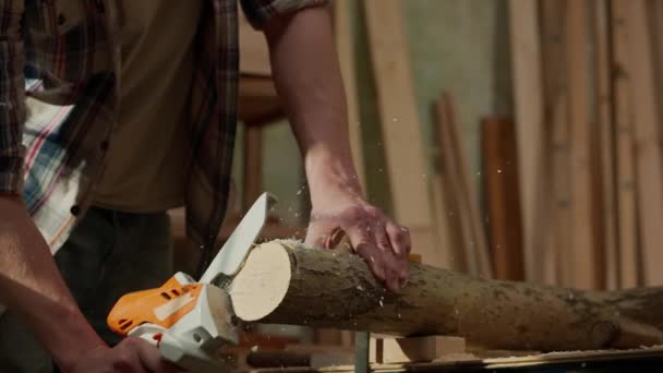カルペントリーと手工芸の広告コンセプト ガレージで働いている男性の木工労働者 コードレスミニチェーンソーを使用して木材のセービング木材で作業する人間の専門の大工 — ストック動画