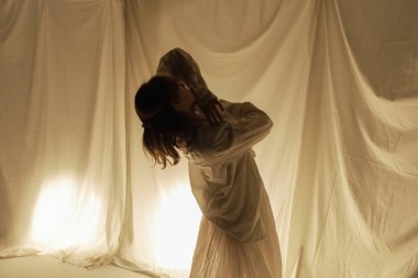 Hafif arka planda dans eden bir dansçının silüeti, akışkan kumaşlarla hareket halinde yakalanır..