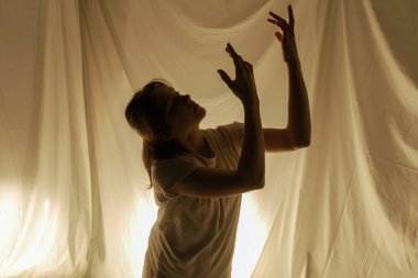 Hafif arka planda dans eden bir dansçının silüeti, akışkan kumaşlarla hareket halinde yakalanır..