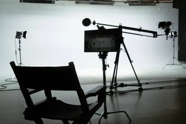 監督の椅子はライトおよびカメラ装置が置かれた専門のフィルムの背景に座りました バックステージショット — ストック写真