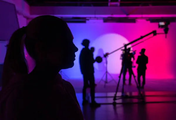 Silhouette profile of a contemplative actress, immersed in colored studio lighting, before the camera rolls. Backstage shot.