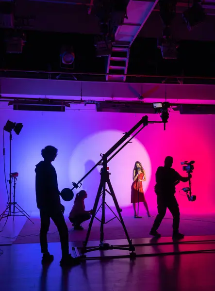 Dynamic film set with a vibrant silhouette of the crew and actress against a colorful backdrop. Backstage shot.