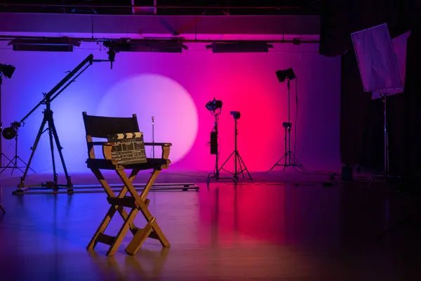 The iconic silhouette of a directors chair stands out in a vividly lit film studio, evoking the creative pulse of movie making. Backstage shot.