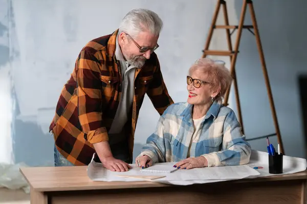 Elderly Couple Blueprints Work Desk Smiling Discussing Home Renovations Retired — Stock Photo, Image