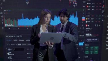 Finansal şirket konsepti. Ofiste başarılı iş adamları. Yatırımcılardan oluşan bir ekip ve CEO büyük dijital ekranların önünde elinde dizüstü bilgisayarla borsa grafikleriyle konuşuyor..