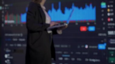 Finansal şirket konsepti. Ofiste başarılı bir iş adamı. Borsa grafikleriyle büyük dijital ekranların önündeki kadın yatırımcı CEO 'su dizüstü bilgisayarla çalışıyor.